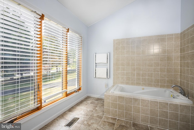 bathroom with a wealth of natural light, vaulted ceiling, and a relaxing tiled tub