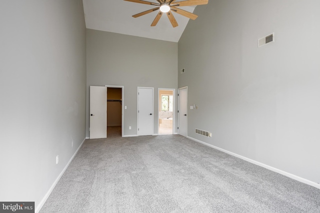 unfurnished bedroom featuring carpet, ceiling fan, high vaulted ceiling, ensuite bathroom, and a walk in closet