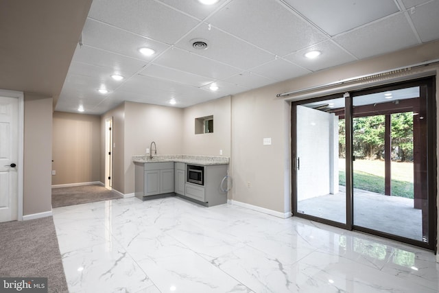 interior space with gray cabinets, stainless steel microwave, sink, and a drop ceiling