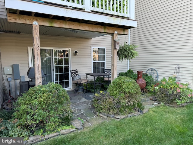 view of exterior entry with a balcony, central air condition unit, and a patio