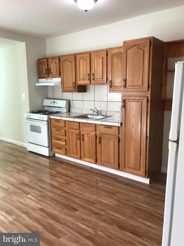 kitchen with decorative backsplash, white appliances, dark wood-type flooring, and sink