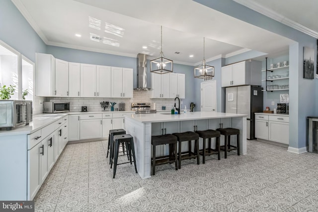 kitchen with a breakfast bar, stainless steel appliances, a kitchen island with sink, wall chimney range hood, and white cabinets