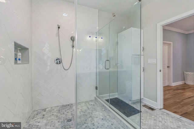 bathroom with wood-type flooring, a shower with shower door, and crown molding