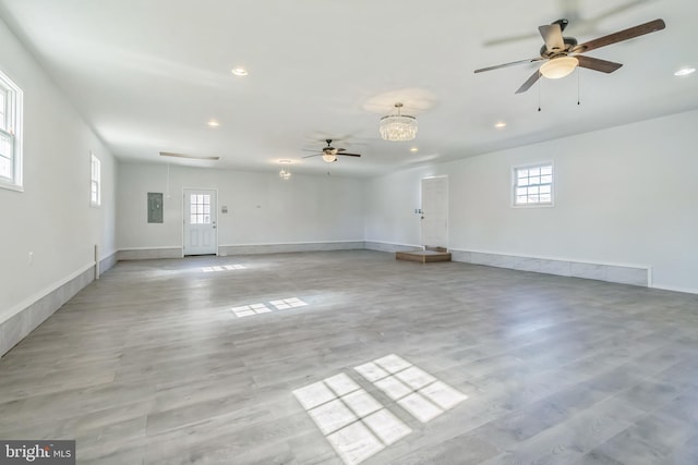 empty room featuring electric panel, light hardwood / wood-style flooring, and ceiling fan with notable chandelier