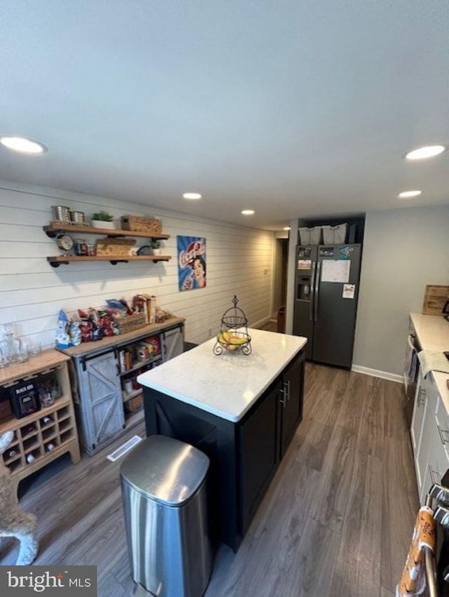 kitchen featuring a center island, dark hardwood / wood-style flooring, wooden walls, and black fridge