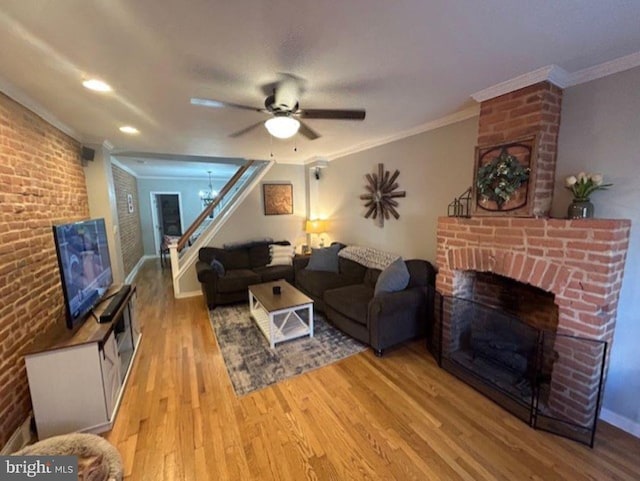 living room with light hardwood / wood-style floors, ornamental molding, brick wall, a fireplace, and ceiling fan with notable chandelier