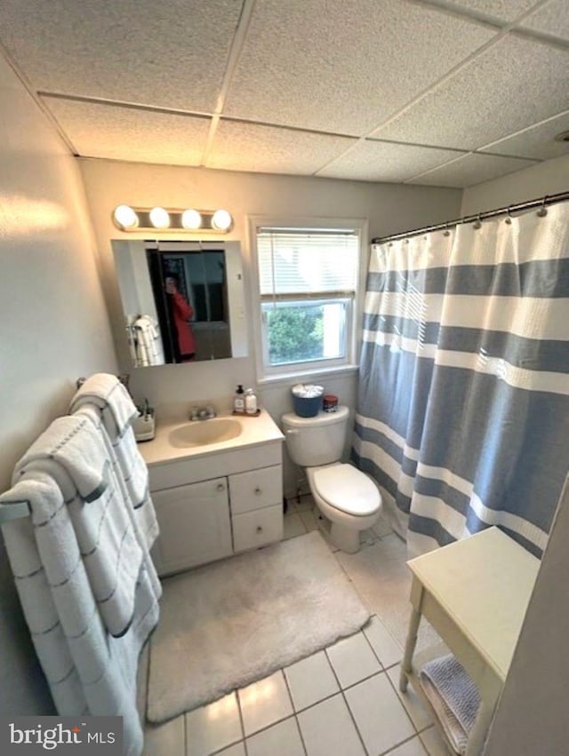 bathroom featuring vanity, toilet, a drop ceiling, and tile patterned flooring