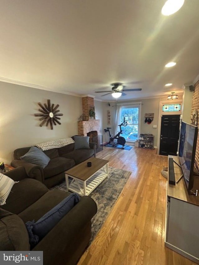 living room with crown molding, a brick fireplace, hardwood / wood-style flooring, and ceiling fan