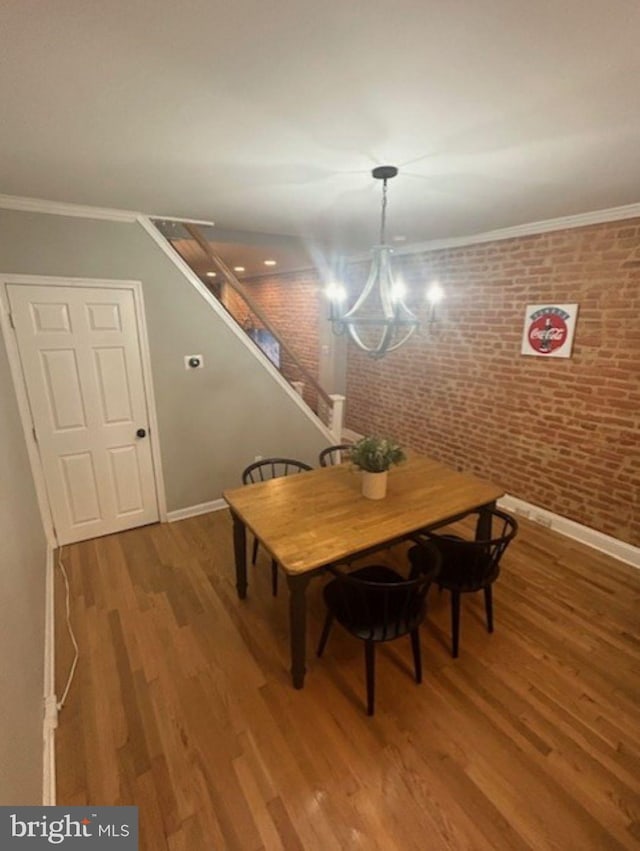 dining room with an inviting chandelier, crown molding, hardwood / wood-style floors, and brick wall