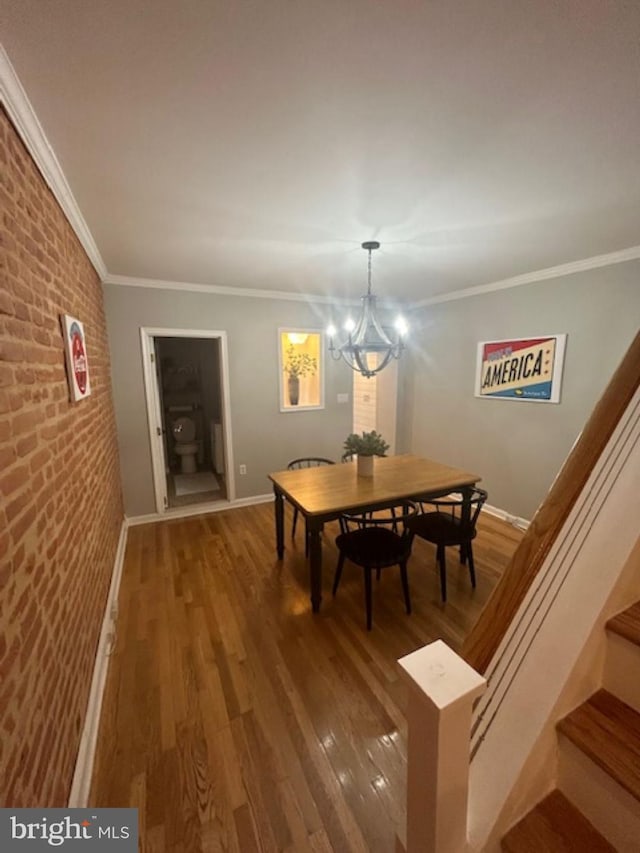 dining space with ornamental molding, hardwood / wood-style floors, a chandelier, and brick wall