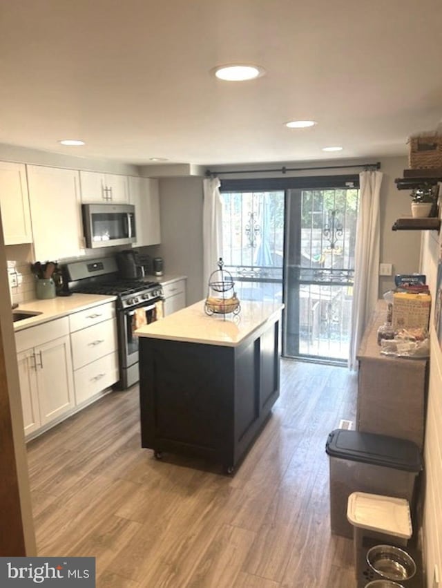 kitchen featuring decorative backsplash, appliances with stainless steel finishes, white cabinetry, wood-type flooring, and a center island