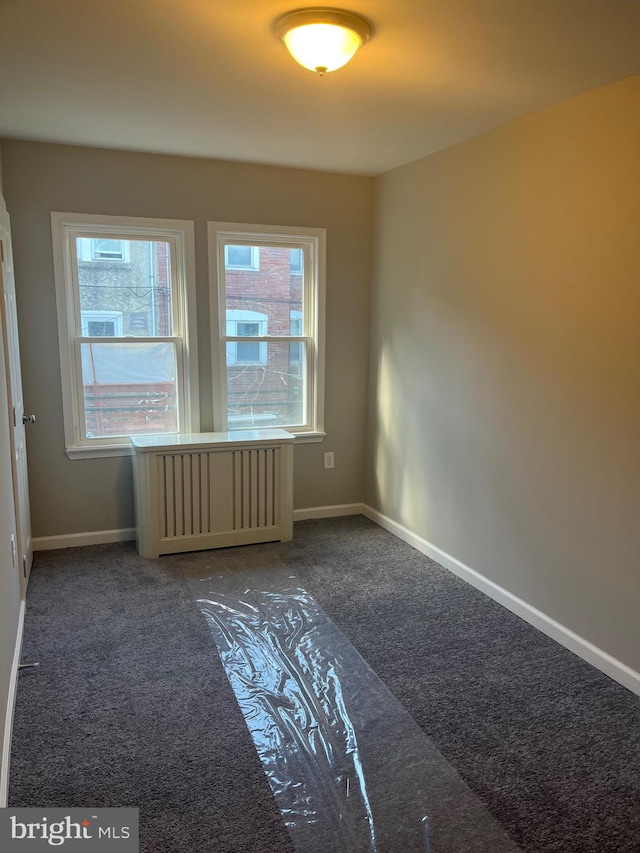 spare room with dark carpet, radiator, and plenty of natural light