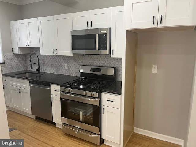 kitchen with tasteful backsplash, appliances with stainless steel finishes, sink, white cabinetry, and light hardwood / wood-style floors