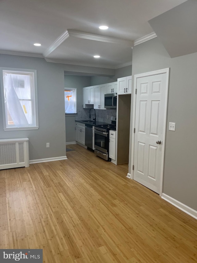 kitchen featuring radiator heating unit, white cabinets, light hardwood / wood-style floors, crown molding, and stainless steel appliances