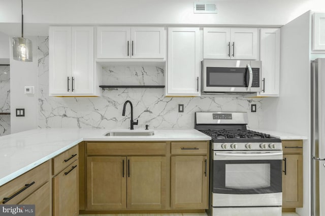 kitchen with sink, appliances with stainless steel finishes, pendant lighting, and white cabinets