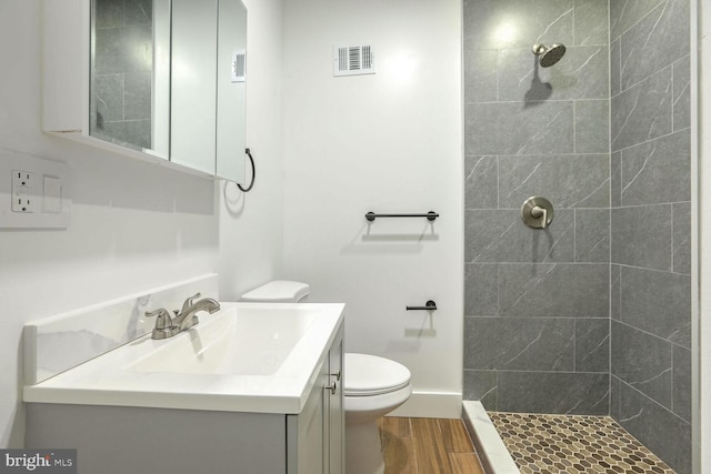 bathroom featuring vanity, a tile shower, wood-type flooring, and toilet