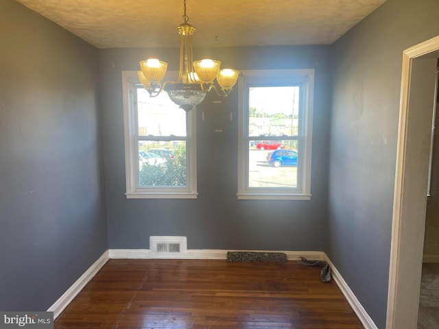 unfurnished dining area featuring dark wood-type flooring, a textured ceiling, and an inviting chandelier