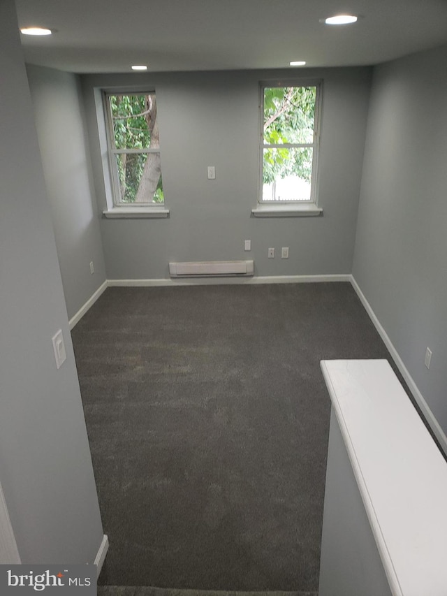 spare room featuring a baseboard heating unit and dark carpet