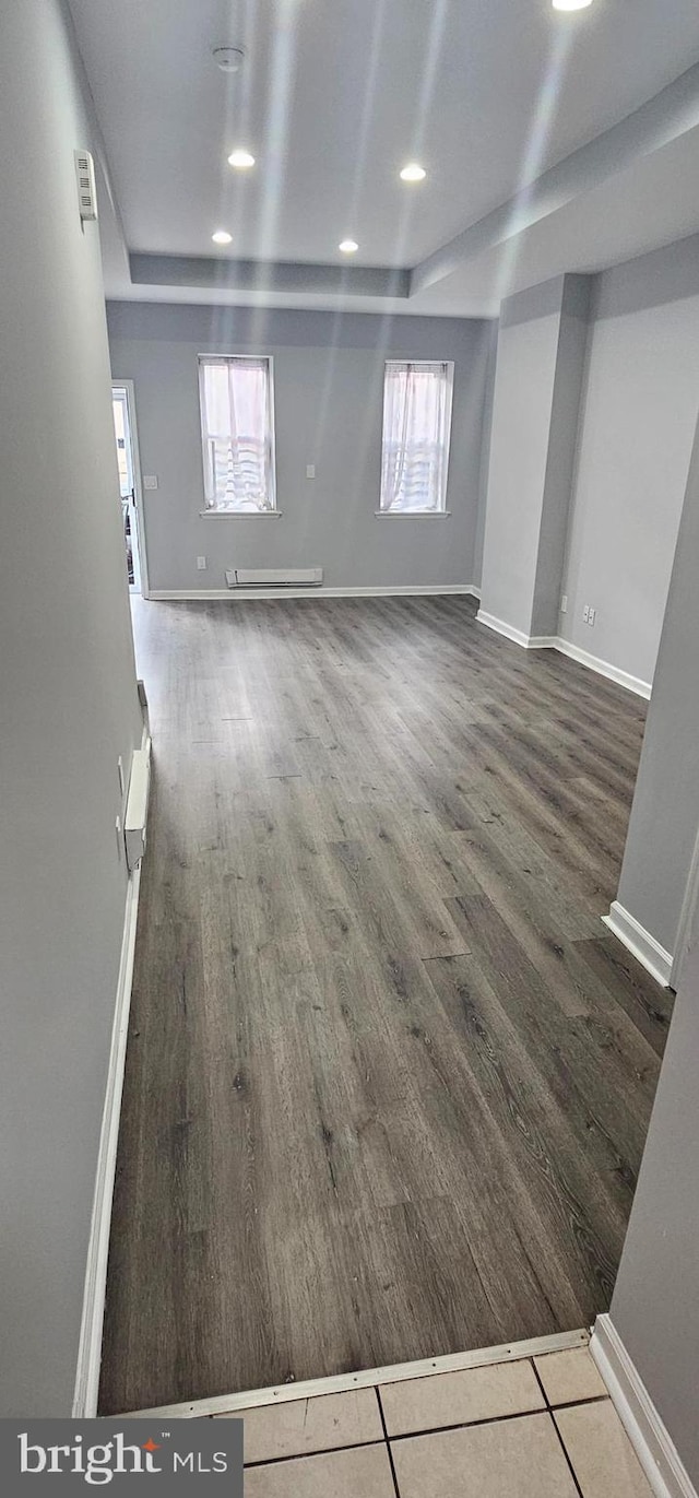 basement featuring baseboard heating, a wealth of natural light, and dark hardwood / wood-style flooring