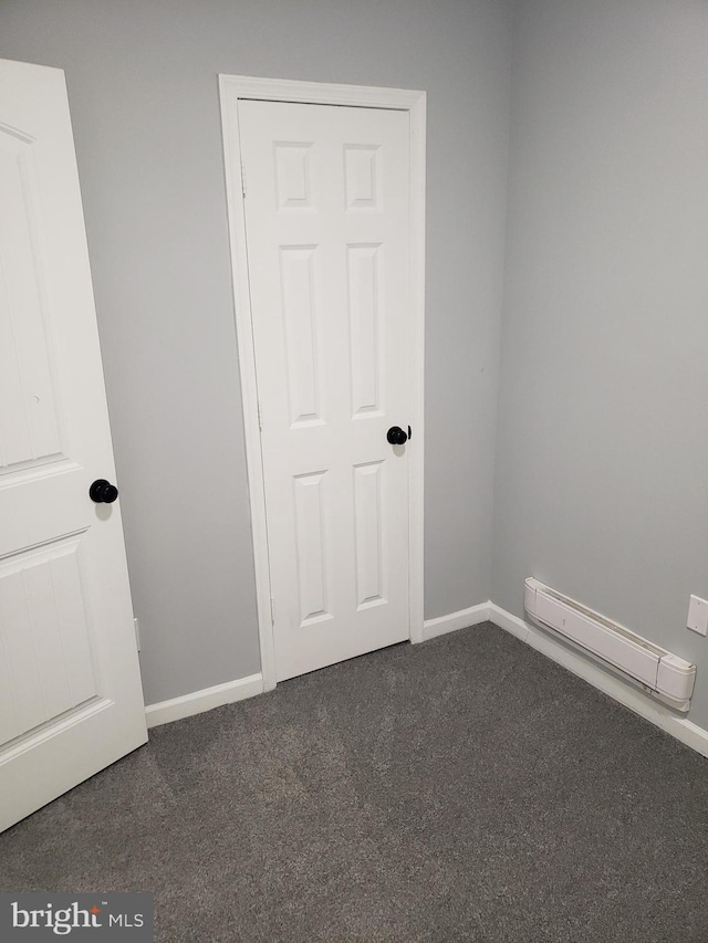 empty room featuring baseboard heating and dark colored carpet