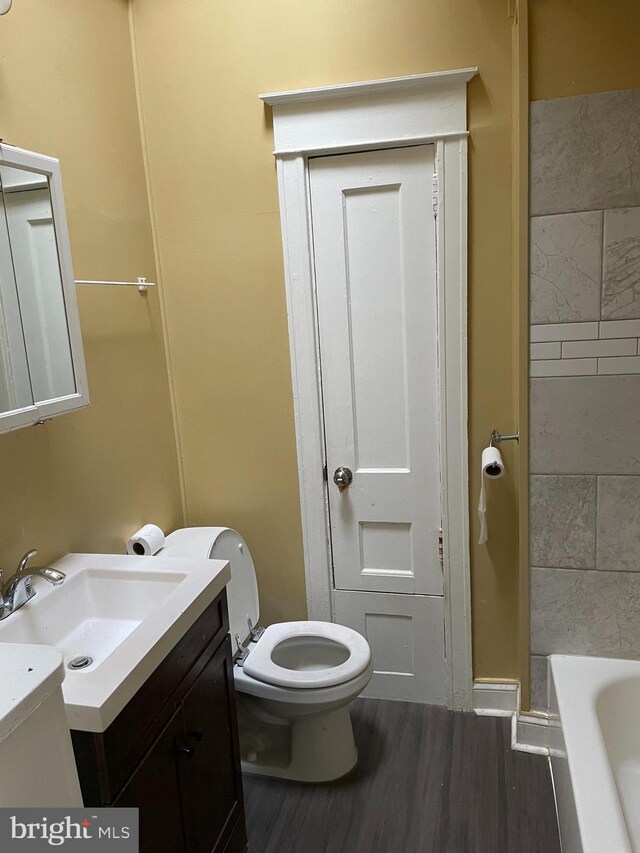 bathroom featuring vanity, toilet, wood-type flooring, and a bath