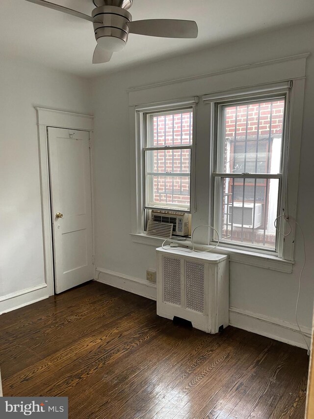 empty room featuring dark wood-type flooring, cooling unit, radiator heating unit, and ceiling fan