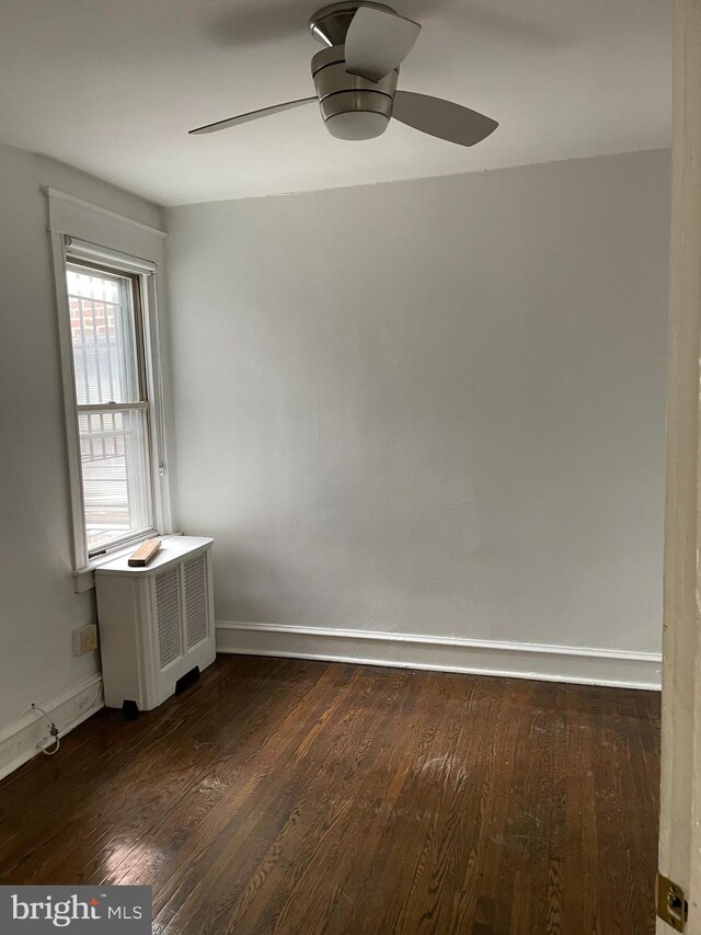 empty room featuring radiator heating unit, ceiling fan, and dark hardwood / wood-style flooring