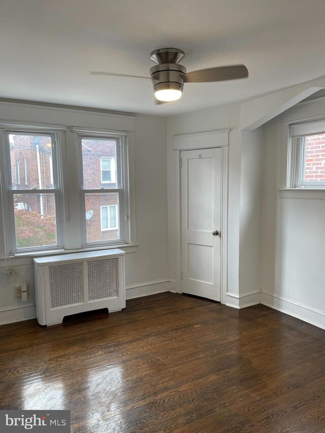 empty room featuring ceiling fan, radiator, and dark hardwood / wood-style flooring