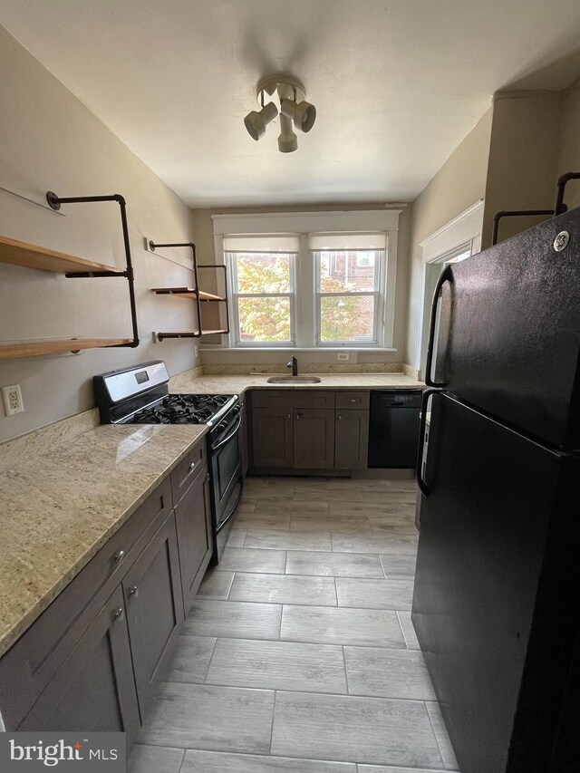 kitchen featuring light stone counters, black appliances, and sink