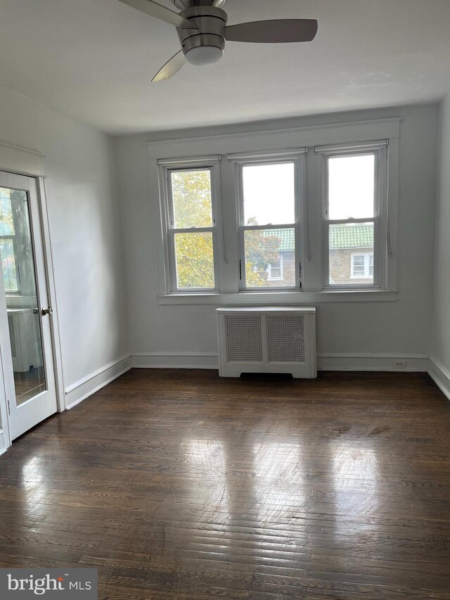 spare room with radiator heating unit, dark wood-type flooring, and ceiling fan