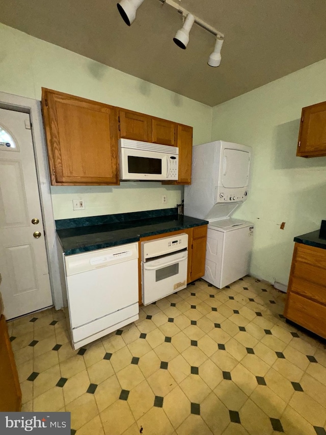 kitchen with rail lighting, stacked washer and clothes dryer, and white appliances