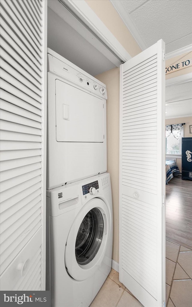 washroom featuring crown molding, light tile patterned flooring, stacked washer and clothes dryer, and a textured ceiling