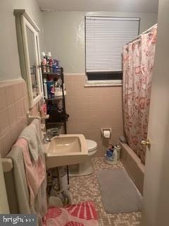 full bathroom featuring shower / bath combo, toilet, sink, and tile walls