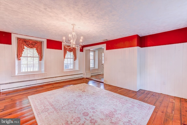 unfurnished dining area featuring a textured ceiling, a baseboard radiator, a chandelier, and hardwood / wood-style floors