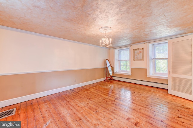 spare room featuring light wood-type flooring, a notable chandelier, ornamental molding, and baseboard heating