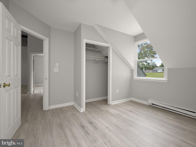 unfurnished bedroom featuring a closet, vaulted ceiling, light hardwood / wood-style flooring, and baseboard heating