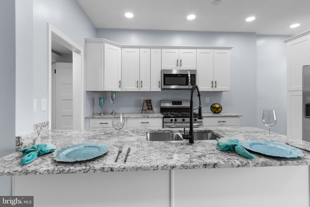 kitchen featuring white cabinetry, sink, light stone counters, kitchen peninsula, and appliances with stainless steel finishes