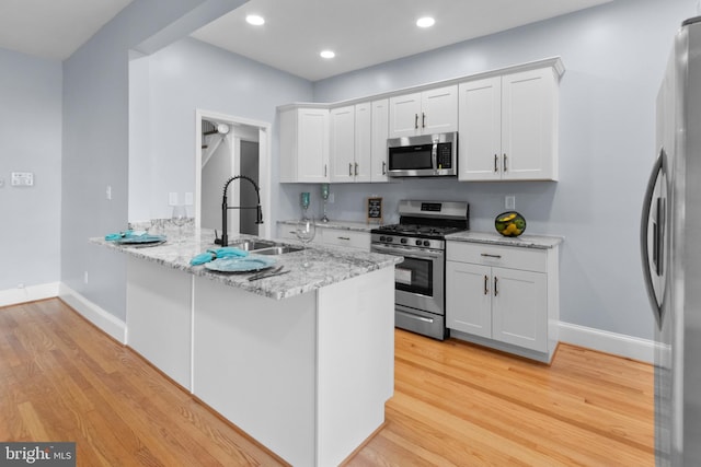 kitchen featuring sink, kitchen peninsula, light stone counters, white cabinetry, and stainless steel appliances