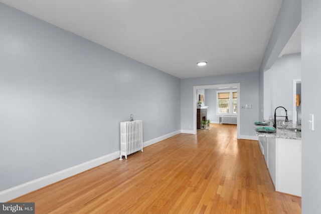 interior space with radiator heating unit, light hardwood / wood-style floors, white cabinetry, and light stone counters