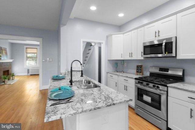 kitchen featuring radiator, white cabinetry, sink, a kitchen island with sink, and appliances with stainless steel finishes