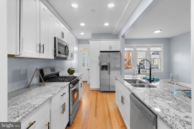 kitchen featuring sink, light stone counters, appliances with stainless steel finishes, white cabinets, and light wood-type flooring