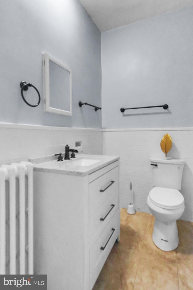 bathroom with radiator heating unit, vanity, tile walls, and toilet