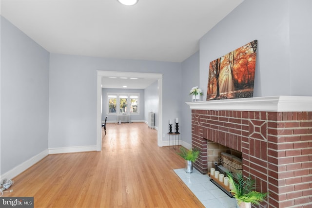 living room featuring radiator heating unit, a fireplace, french doors, and light wood-type flooring