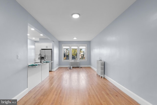 unfurnished living room featuring radiator heating unit and light hardwood / wood-style flooring