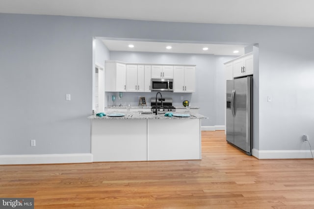 kitchen with white cabinets, appliances with stainless steel finishes, light hardwood / wood-style floors, light stone counters, and kitchen peninsula