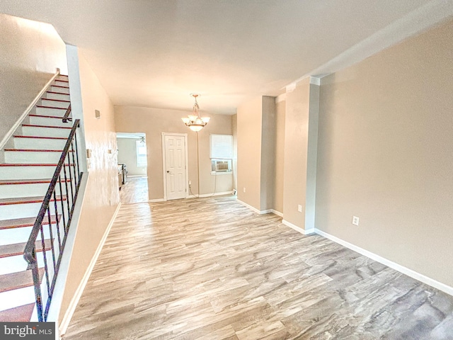 unfurnished living room with cooling unit, a notable chandelier, and light wood-type flooring