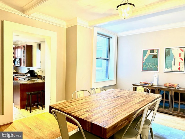 dining area featuring light hardwood / wood-style floors, beamed ceiling, ornamental molding, and sink