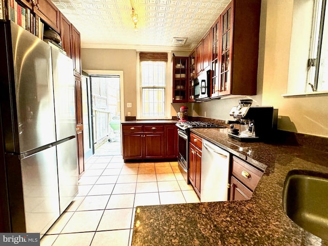 kitchen with sink, light tile patterned floors, appliances with stainless steel finishes, dark stone countertops, and crown molding