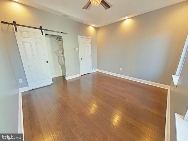 unfurnished bedroom featuring a barn door, ceiling fan, and dark hardwood / wood-style flooring