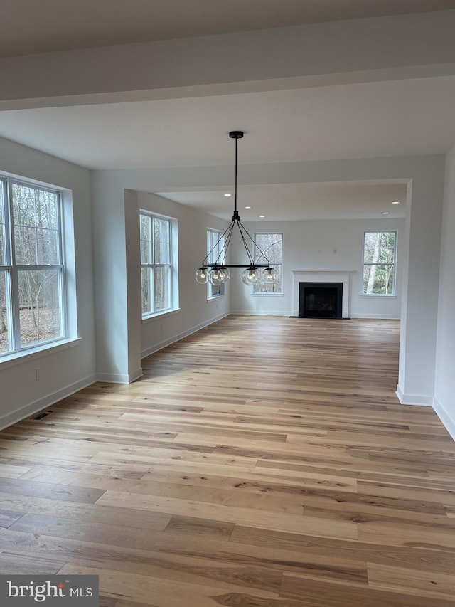 unfurnished living room with light hardwood / wood-style flooring, a healthy amount of sunlight, and a notable chandelier